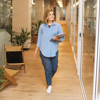 Eine junge Frau geht mit Unterlagen in der Hand über einen Büroflur.