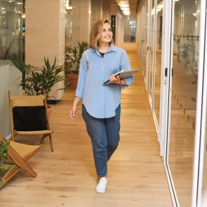 Eine junge Frau geht mit Unterlagen in der Hand über einen Büroflur.